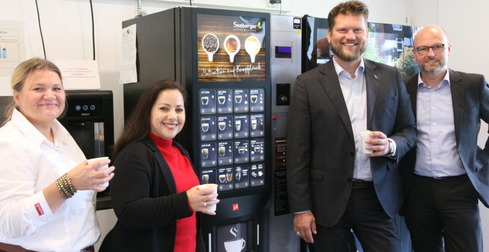 Personen mit Kaffeebechern vor einem Vendingautomat