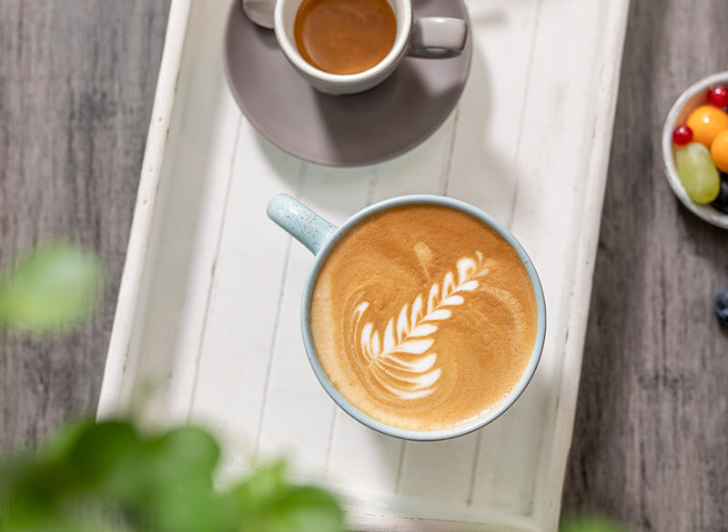 Cappuccino mit Latte Art Blatt mit Espressi auf einem Holztablett