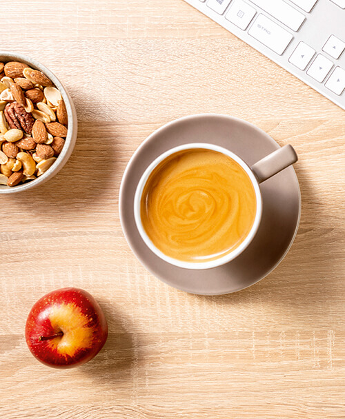 Arbeitsplatz mit Kaffee, Apfel, Snacks und Tastatur