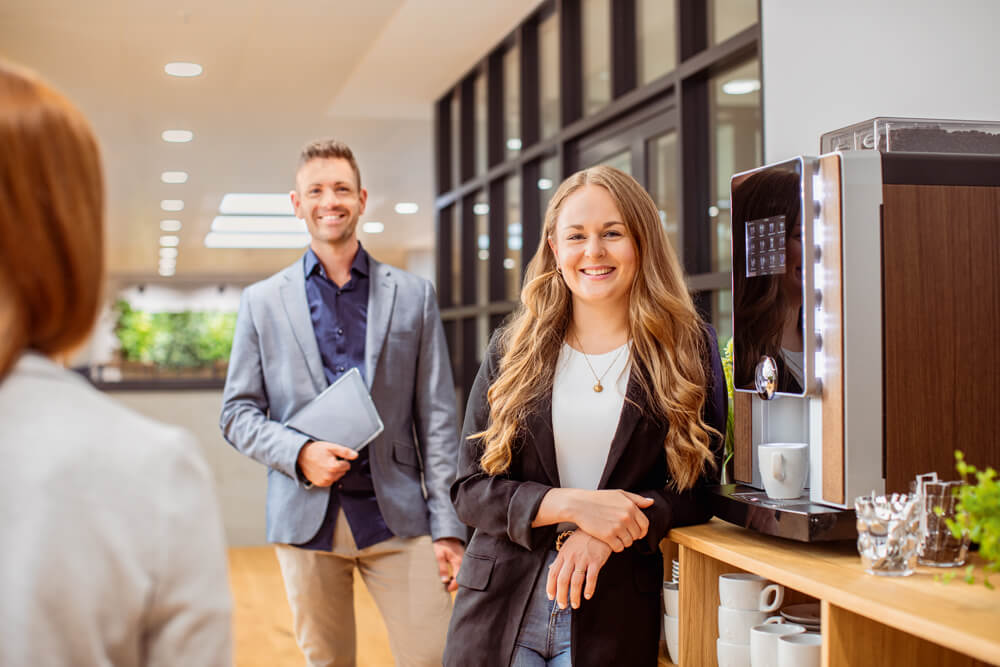 Mitarbeitende vor einem Kaffeevolautomat im Büro