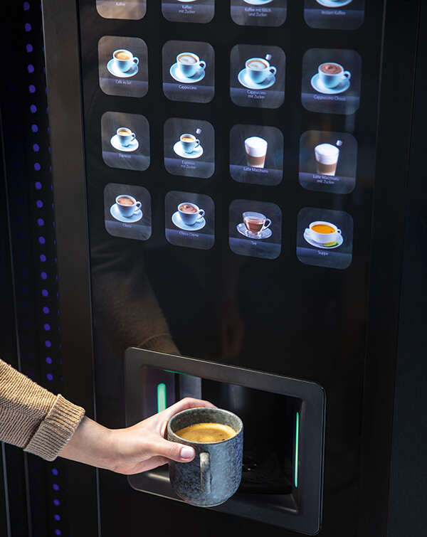 Person entnimmt Kaffee am Vendingautomat