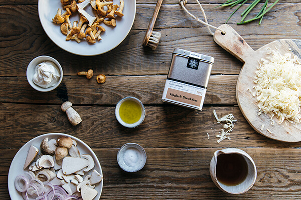 flammkuchen-english-breakfast-zutaten Samova Tee auf Holztisch, daneben Gemüse, Käse und Kaffee
